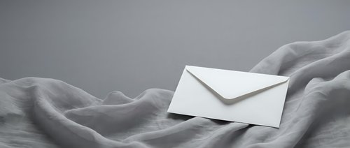White envelope resting on soft gray fabric with elegant folds and shadows, minimalist composition for correspondence and communication concepts.