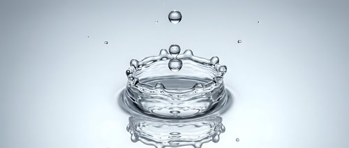 Water drop creating crown splash with ripples on reflective surface against clean white background for commercial design projects.