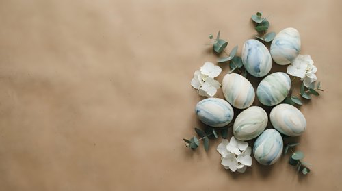 Easter eggs decorated in soft green and white tones with eucalyptus branches and flowers on beige background for spring holiday celebration.
