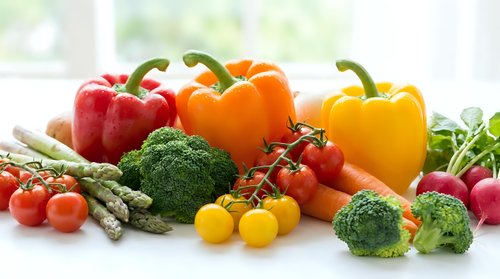 Fresh colorful vegetables including bell peppers, broccoli, tomatoes, asparagus and radishes arranged on white surface for healthy cooking and nutrition.
