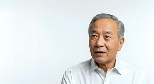 Senior Asian man with gray hair wearing light blue button-up shirt, looking thoughtfully to the side against white background for corporate and lifestyle use.