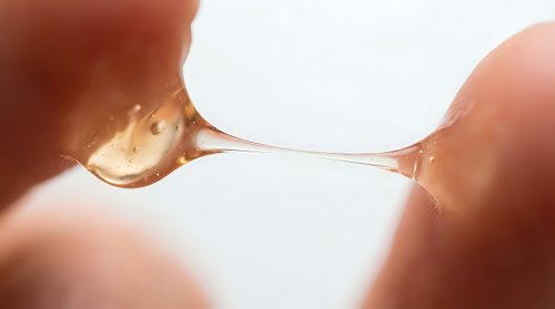Macro shot of liquid droplet suspended between two fingers against bright backlit background, showcasing surface tension and fluid dynamics for scientific and educational content.