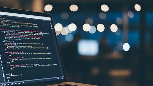 Software developer programming code on laptop screen in modern office environment with bokeh lights background for technology projects.