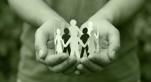Protective hands holding paper cutout family figures symbolizing care, support, unity and social responsibility in community welfare concept.