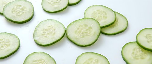 Fresh cucumber slices arranged on white background, healthy vegetable ingredient for salads, cooking and food preparation in kitchen.