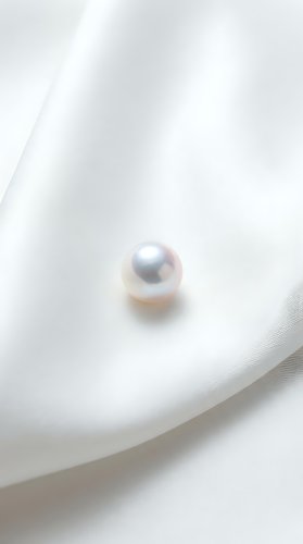Single lustrous pearl resting on soft white fabric with gentle folds, showcasing luxury jewelry and elegant design elements for premium branding.