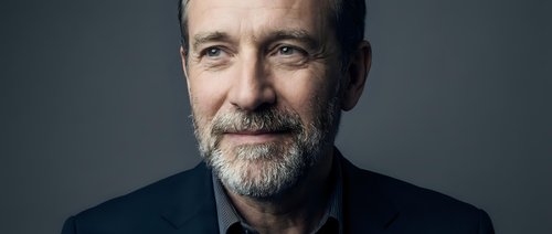 Middle-aged man with salt-and-pepper beard wearing dark blazer against neutral background. Professional portrait for corporate, business, and executive headshot applications.