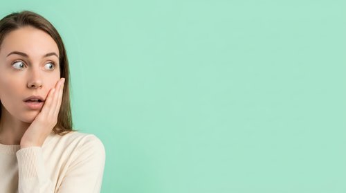 Surprised young woman with hand on face against mint green background, expressing shock and astonishment for advertising and marketing campaigns.