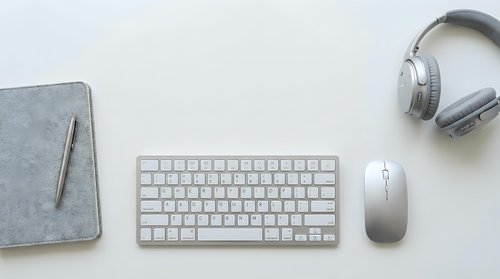 Minimalist workspace flat lay with wireless keyboard, mouse, headphones, and felt notebook on white background.