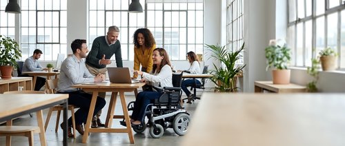 Diverse business team collaborating in modern office with wheelchair user promoting workplace inclusion and accessibility for corporate presentations.