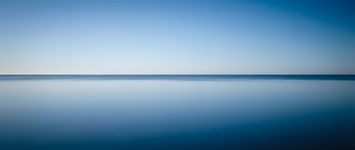 Serene ocean horizon with calm blue waters reflecting clear sky in minimalist seascape composition for meditation and wellness backgrounds.