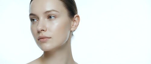 Young Caucasian woman with natural makeup and glowing skin looking sideways on white background for skincare and beauty advertising campaigns.