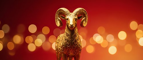 Golden ram figurine with curved horns against warm red and orange bokeh background, suitable for luxury branding, festive celebrations, and premium design projects.