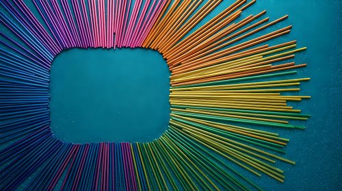 Colorful rainbow gradient rays burst from central teal square frame on textured blue background creating dynamic radial sunburst pattern for modern design projects.