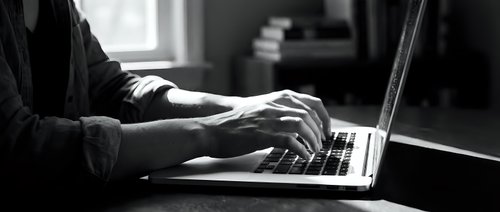 Professional businessman typing on laptop computer in modern office workspace with natural window lighting for remote work and business productivity.