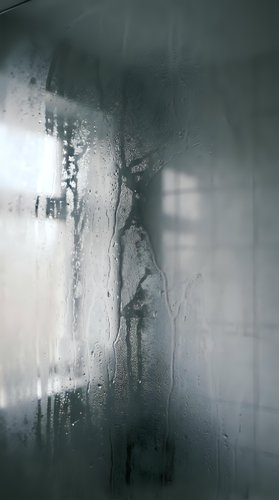 Water droplets and condensation on glass shower door creating abstract patterns with blurred bathroom background for spa and wellness concepts.
