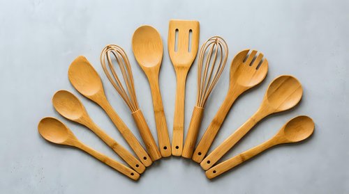 Wooden kitchen utensils set arranged in fan pattern on gray background. Natural bamboo cooking tools for culinary preparation and food service.