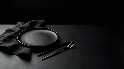Empty plate with fork and knife on dark surface with fabric napkin, minimalist table setting for restaurant, dining, or food service design projects.
