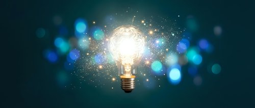 Glowing light bulb with sparkling particles and blue bokeh lights on dark background symbolizing creativity, innovation and bright ideas for business concepts.