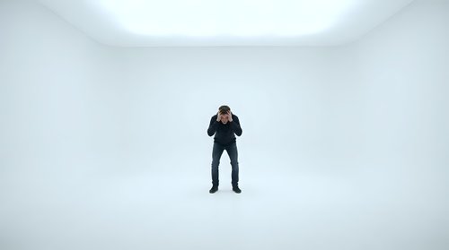 Businessman in dark suit standing alone in empty white minimalist room with clean walls and bright lighting for corporate and professional concepts.