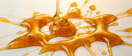 Liquid amber or honey splashing and dripping with dynamic motion, creating an abstract golden splash pattern against a white background for design and creative projects.