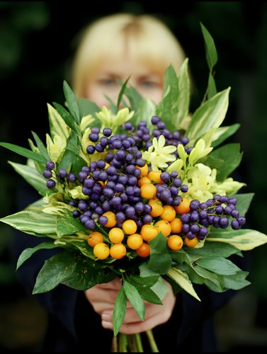 Woman holding autumn bouquet with purple and orange berries surrounded by green foliage for seasonal decoration and floral arrangements.