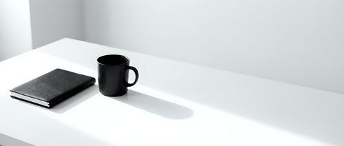 Minimalist workspace with black mug and notebook on white desk, monochrome office setup for business, productivity, and creative work environments.