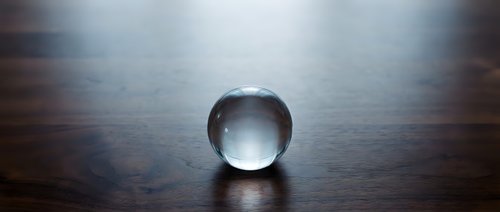 Clear glass crystal ball sphere sitting on dark wooden surface with dramatic lighting and shadows creating mystical atmosphere for fortune telling divination.
