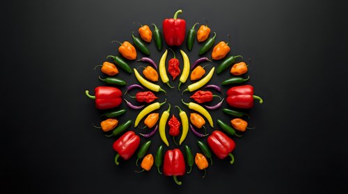 Colorful bell peppers arranged in symmetrical mandala pattern on dark background for healthy eating and vegetarian cooking concepts.