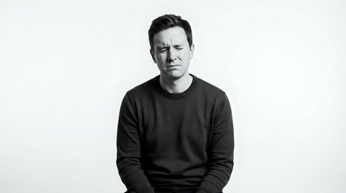Professional Caucasian man in dark sweater sitting confidently against white background, business portrait for corporate branding and marketing materials.