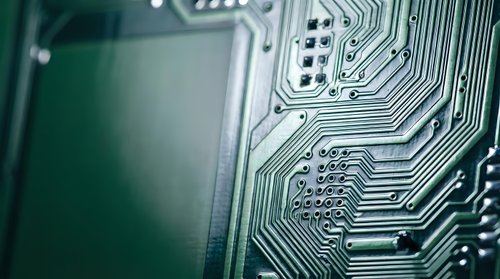 Green circuit board with intricate electronic pathways and microchip components for technology and computing applications.
