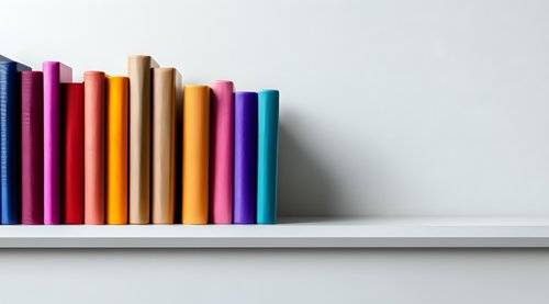 Colorful book spines arranged in rainbow order on white shelf against neutral wall, creating minimalist composition for education and learning concepts.