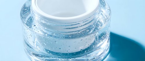 Clear glass cosmetic jar with white lid containing blue skincare cream or gel product on clean background for beauty and wellness applications.