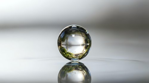 Transparent glass sphere with golden yellow tint reflecting on glossy surface creating mirror effect against soft gradient background for luxury design concepts.