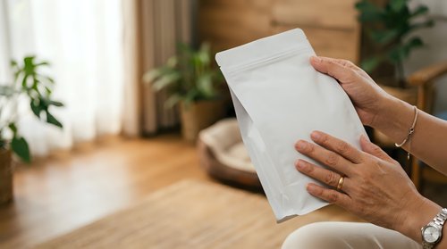 Woman holding blank white envelope in modern living room with plants and natural light, suitable for mail, correspondence, invitation, and business communication concepts.
