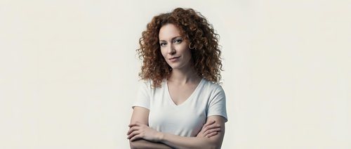 Confident young woman with curly hair and crossed arms on neutral background for business and professional marketing materials.