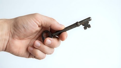 Hand holding vintage rusty metal key on white background, isolated object for security, access, unlock, antique, mystery, real estate concepts.