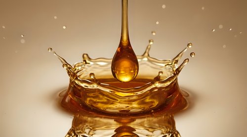 Golden honey drop falling and creating a crown splash, captured in macro detail with warm amber tones for food, beauty, and wellness concepts.