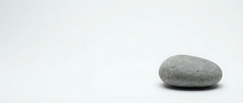 Single smooth gray stone on clean white background for zen meditation spa wellness design projects.