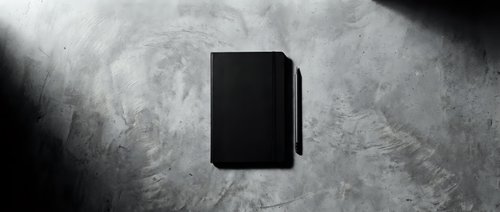 Black book or notebook on grunge concrete surface with dramatic lighting, suitable for publishing, education, and stationery design projects.