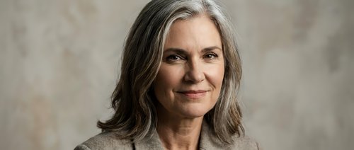 Mature woman with long gray hair and fair complexion smiling at camera against neutral background, suitable for healthcare, wellness, lifestyle and corporate business applications.