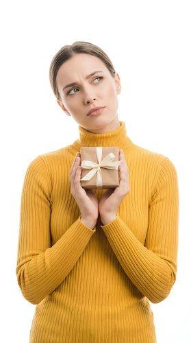 Young woman with light skin tone and brown hair wearing mustard yellow ribbed turtleneck sweater, holding wrapped gift box with bow, isolated on white background for holiday and celebration concepts.
